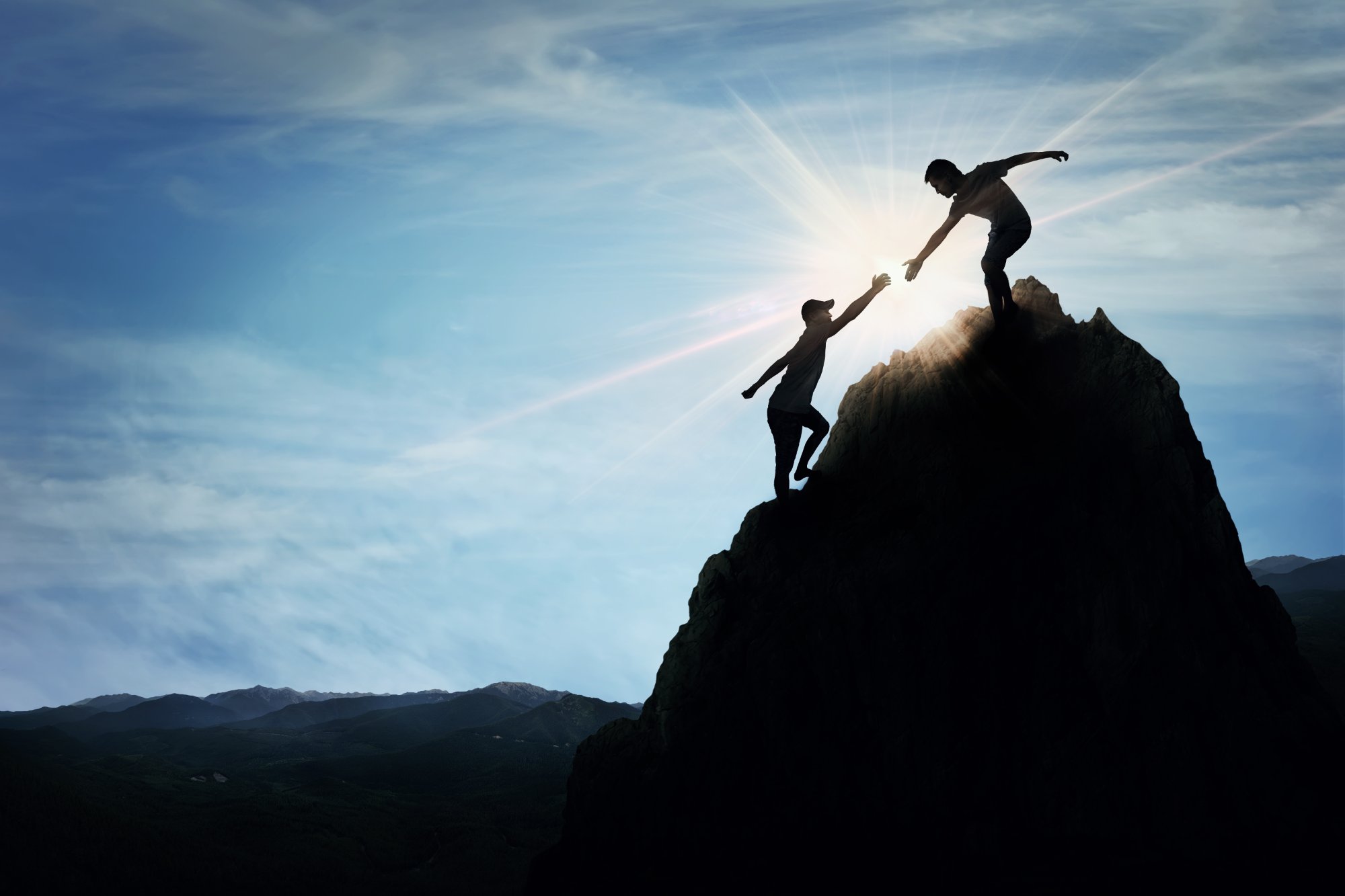 Two people on a mountain, one reaching down to help the other up